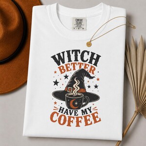 Può includere: Una t-shirt bianca a girocollo con la grafica di un cappello da strega nero e una tazza di caffè fumante. Il testo WITCH BETTER HAVE MY COFFEE è scritto in nero e arancione, circondato da piccole stelle e da una luna crescente.