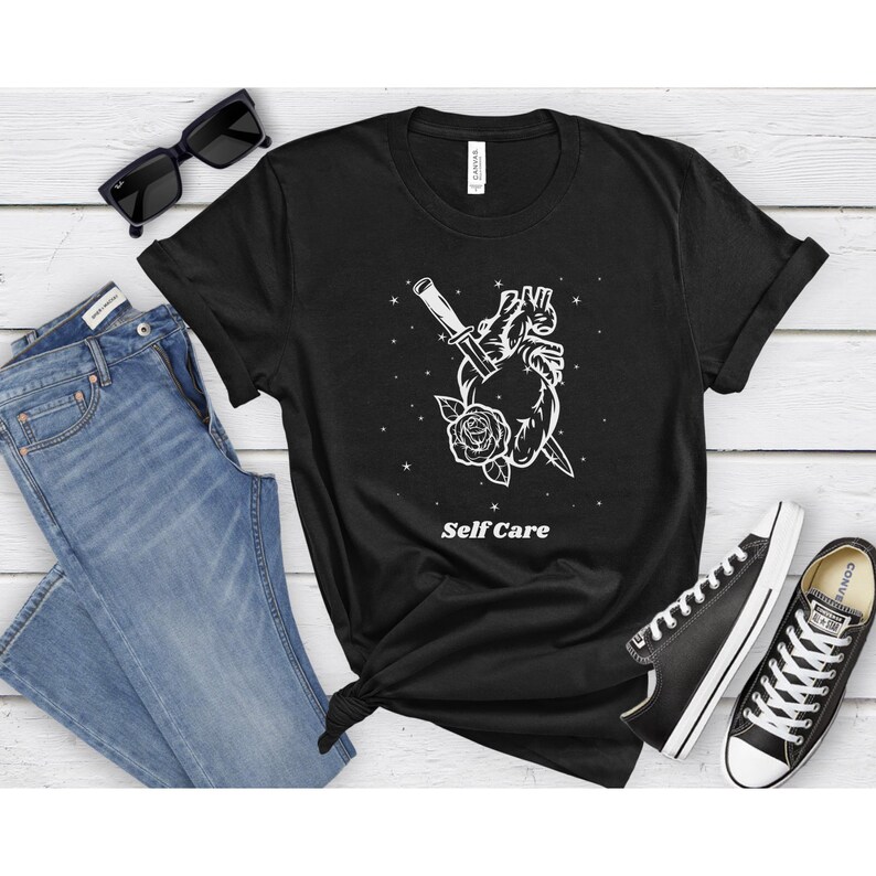 May include: Black t-shirt with a white graphic of a heart pierced by a knife and a rose. The text "Self Care" is printed below the graphic.