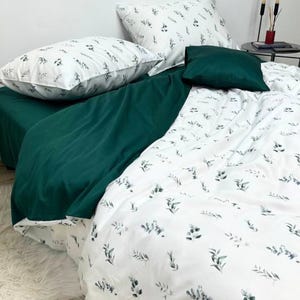 Könnte beinhalten: Ein weißes Bettwäsche-Set mit einem grünen Blatt-Muster. Das Set beinhaltet einen Bettbezug, zwei Kissenbezüge und ein Dekokissen. Der Bettbezug und die Kissenbezüge haben einen weißen Hintergrund mit einem dezenten grünen Blatt-Muster. Das Dekokissen ist einfarbig grün.