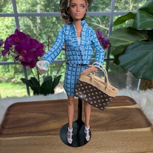 May include: A doll in a blue and white patterned blazer and skirt, holding a Starbucks coffee cup and a brown handbag with a star pattern. The doll wears white heels and a black belt.