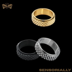 Peut inclure: Trois bagues rotatives en acier inoxydable, dorées, noires et argentées. Les bagues présentent un motif texturé en forme d'écailles sur la bande extérieure. Le mot "SENSORIALLY" est au bas de l'image.