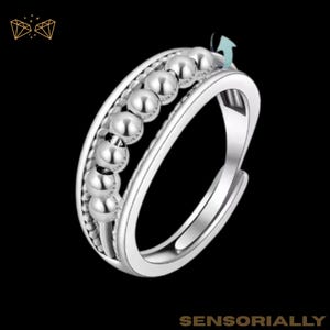 May include: A silver-colored fidget ring with a row of small, round beads that spin freely. The ring has a sleek, modern design with a polished finish. The word "SENSORIALLY" is printed at the bottom of the image.