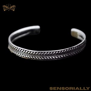 May include: A silver cuff bracelet with a detailed leaf pattern. The open-ended bracelet has a textured design that wraps around the wrist. The bracelet is displayed against a black background.