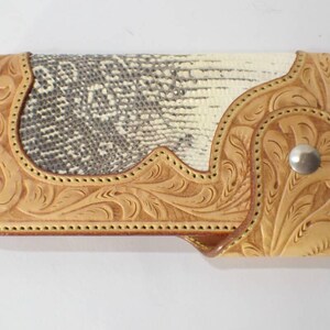 Può includere: Un portafoglio in pelle fatto a mano con un motivo a pelle di serpente e intricate decorazioni floreali. Il portafoglio presenta un colore marrone chiaro con una chiusura a scatto argentata. Il design mostra una miscela di trame naturali e artigianato dettagliato.
