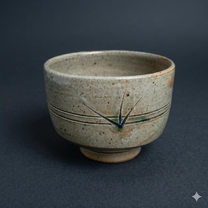 May include: A handmade ceramic bowl with a speckled, beige glaze. The bowl features two horizontal lines and a decorative starburst design. The bowl has a small, circular base and is suitable for serving food or as a decorative piece.