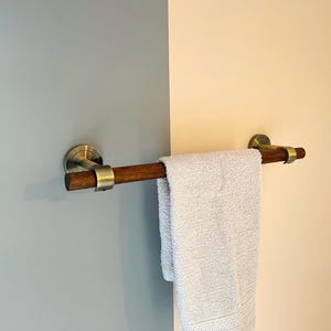 Peut inclure: Un porte-serviettes en bois avec des fixations en laiton monté sur un mur. Une serviette blanche est accrochée à la barre.