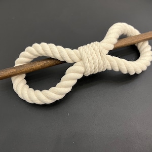 Op de afbeelding: Een wit katoenen touw haarband met een houten stokje erdoorheen. Het touw is in een knoop geknoopt en het stokje is aan beide uiteinden zichtbaar.