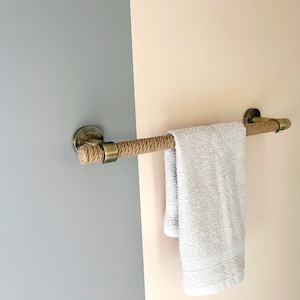 Puede incluir: Un toallero de cuerda con tapas de latón en los extremos, montado en una pared con pintura de dos tonos. Una toalla blanca cuelga del toallero.