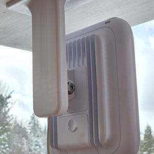 May include: A white, ceiling-mounted device with a rectangular body and a series of vertical ridges. The device is attached to a white bracket that is mounted to the ceiling. A cable extends from the device. The background shows a snowy landscape.