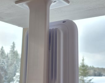 May include: A white, rectangular ceiling mount with a vertical support and a rounded, rectangular device attached. The device has a series of vertical ridges on its side. The mount is attached to a white wooden surface.
