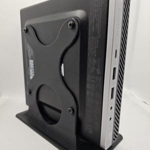 Könnte beinhalten: Ein schwarzer Desktop-Computerständer mit einem silbernen HP-Desktop-Computer, der daran befestigt ist. Der Ständer hat einen runden Ausschnitt auf der Rückseite und ist mit vier Schrauben am Computer befestigt.