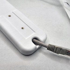 May include: White plastic cable management clip with two screws. A gray ethernet cable is threaded through the clip. The cable is labeled "EIA-568-B-2 CAT"