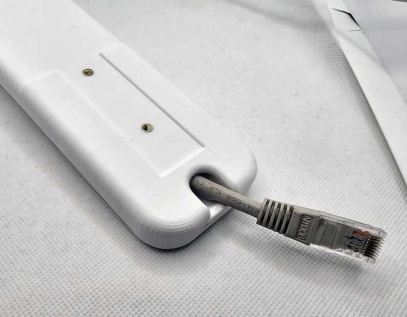 May include: White plastic cable management clip with two screws. A gray ethernet cable is threaded through the clip. The cable is labeled "EIA-568-B-2 CAT"
