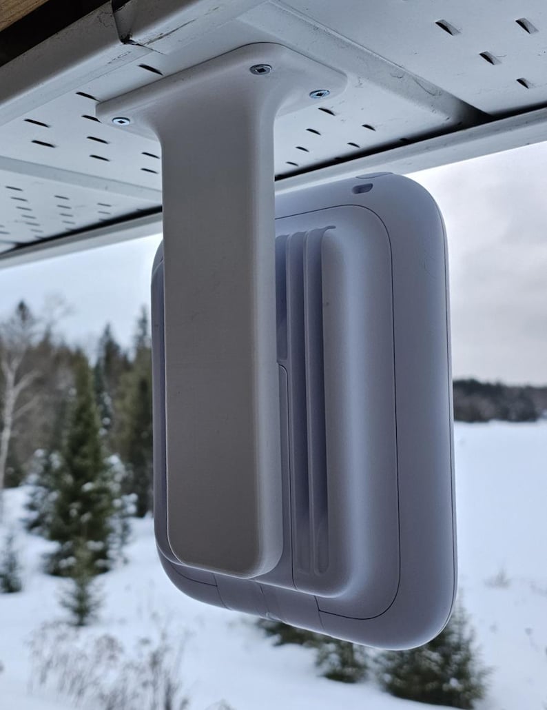 May include: White security camera mounted on a white bracket attached to a white soffit. The camera is facing forward and the bracket is facing the side. The camera is mounted on the outside of a building.