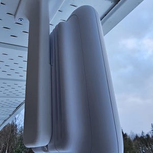 May include: White outdoor security camera mounted on a white bracket attached to a white ceiling. The camera is facing downwards.