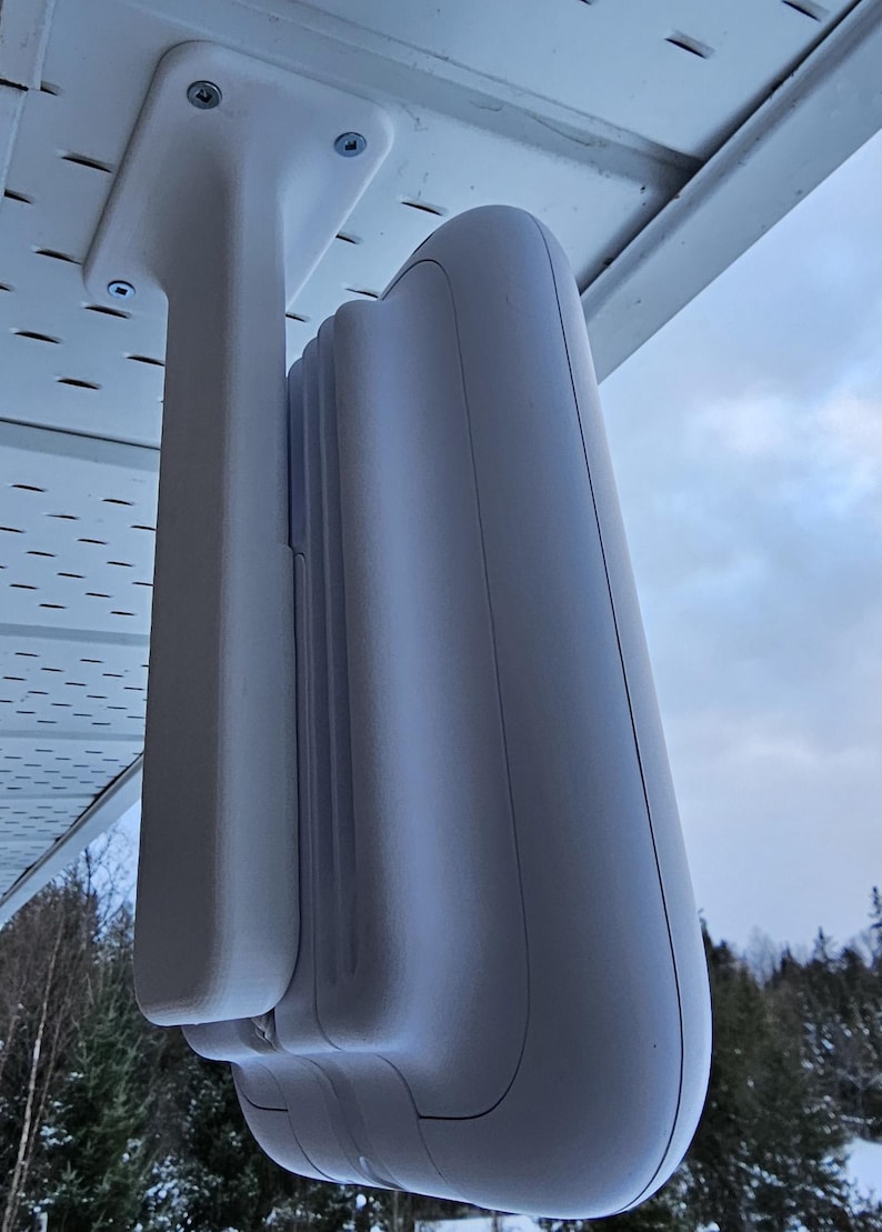 May include: White outdoor security camera mounted on a white bracket attached to a white ceiling. The camera is facing downwards.