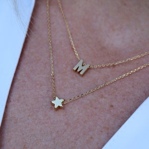 May include: A gold chain necklace with a star charm and a letter 'M' charm.