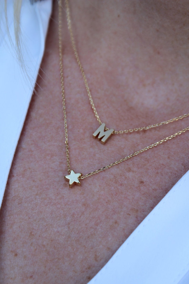 May include: A gold chain necklace with a star charm and a letter 'M' charm.