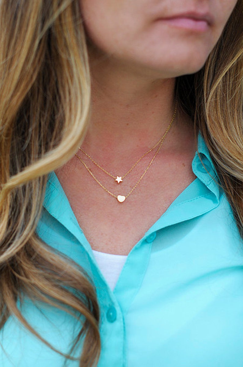 May include: A woman wearing a turquoise shirt with a gold chain necklace featuring a small star and heart pendant.