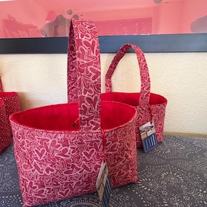 Peut inclure: Des paniers en tissu rouge avec des motifs de cœurs. Les paniers ont un intérieur rouge et des poignées assorties. Le tissu présente un motif de cœur blanc sur fond rouge. Les paniers sont de tailles variables.