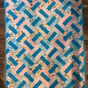 May include: A handmade quilt with a repeating pattern of turquoise rectangles and floral and pink patterned fabric. The quilt has a turquoise border and is likely made of cotton. The design is a modern take on a traditional quilt.