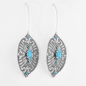 May include: A pair of silver-toned drop earrings featuring an intricate filigree marquise-shaped frame. Each earring is centered with an oval turquoise-colored stone and accented with smaller round turquoise-colored beads along the metal structure.