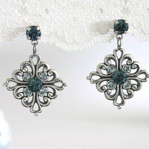 Peut inclure: Boucles d'oreilles en filigrane argent avec un cristal bleu sarcelle au centre et de plus petits cristaux clairs autour.