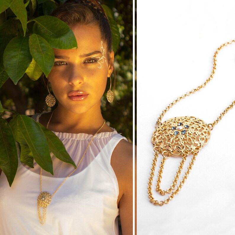 May include: A gold necklace with a large, ornate pendant featuring a delicate filigree design and blue gemstones. The pendant hangs from a chain with three strands of smaller chains.
