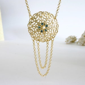 May include: A gold necklace with a large, round pendant featuring a delicate filigree design and blue and white gemstones.