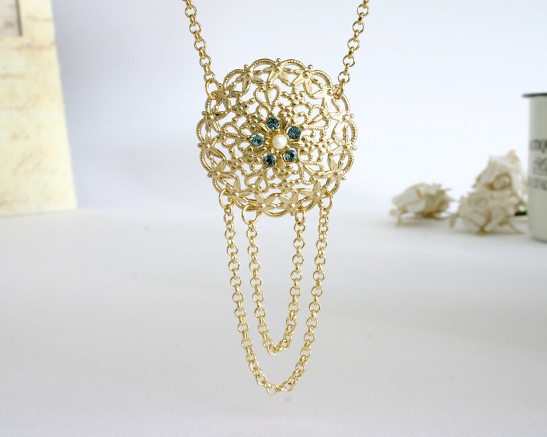 May include: A gold necklace with a large, round pendant featuring a delicate filigree design and blue and white gemstones.
