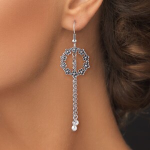 May include: Silver dangle earrings with a circle design featuring small flower accents and a chain with two pearl-like beads at the bottom.