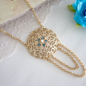 May include: A gold necklace with a round pendant featuring a delicate filigree design and blue and white gemstones.