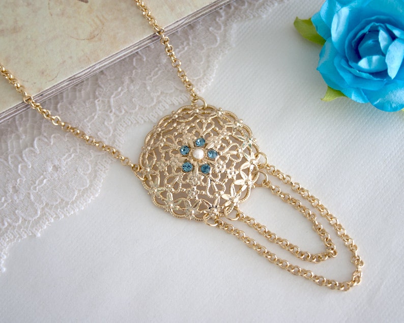 May include: A gold necklace with a round pendant featuring a delicate filigree design and blue and white gemstones.
