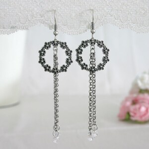 May include: Silver dangle earrings with a circle of small black flowers and a chain with a clear crystal at the end.