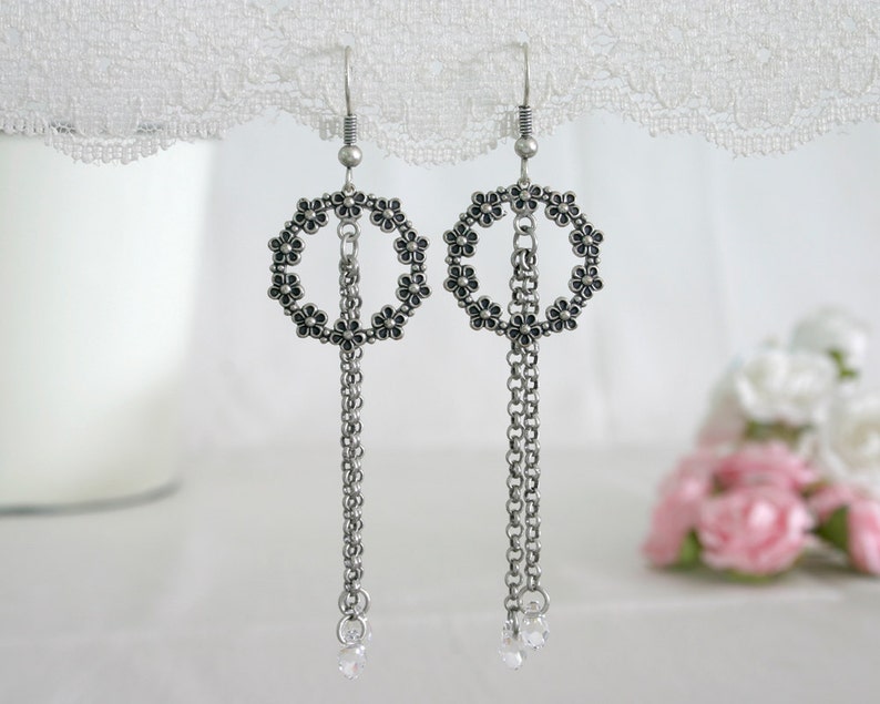 May include: Silver dangle earrings with a circle of small black flowers and a chain with a clear crystal at the end.