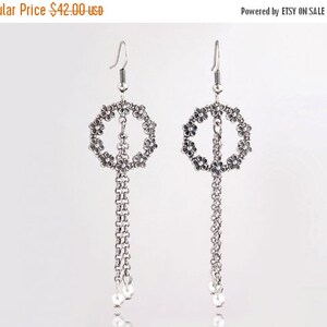 May include: Silver dangle earrings with a circle of small flower designs and a chain with a pearl at the end.