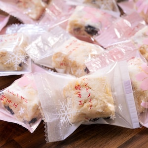 May include: Individually packaged white nougat candy with a snowflake design on the packaging. The candy is wrapped in clear plastic with a pink backing. The packaging has Japanese text that reads "Nougat with a snowflake design".