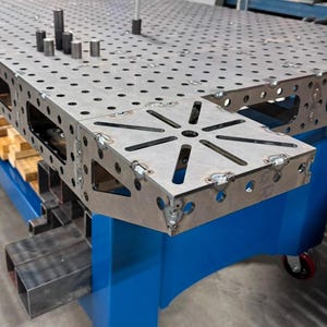 Może przedstawiać: Stalowy stół spawalniczy w kolorze niebieskim z powierzchnią kratową i obrotową platformą. Stół ma niebieską podstawę i koła.