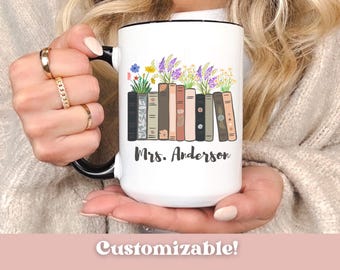 May include: White ceramic mug with a black handle and rim, featuring a design of books with flowers on top. The mug has the name "Mrs. Anderson" printed on it. The word "Customizable!" is at the bottom.