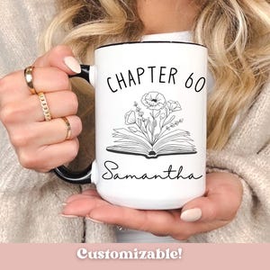 May include: White ceramic mug with black handle and rim. The mug features the text "CHAPTER 60" above an open book illustration with floral accents. The name "Samantha" is written below the book. The word "Customizable!" is at the bottom.