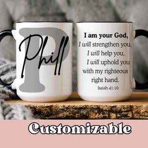 May include: Two white ceramic mugs with black handles and rims. One mug features the name "Phill" in a script font over a gray "P". The other mug has a Bible verse printed on it. The word "Customizable" is at the bottom.