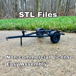 以下が含まれることがあります： 2つの車輪、ヒッチ、サポートレッグを備えた黒いモデルトレーラー。「STL Files」の文字が上部にあり、その下に「Non-commercial License」と「Easy Assembly」の文字があります。