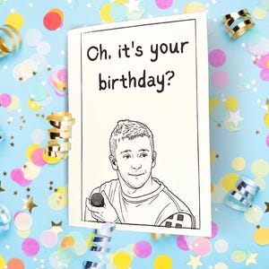 May include: A white greeting card with a black line drawing of a person holding a microphone. The text at the top reads, Oh, it's your birthday? The card is centered against a light blue background covered in colorful confetti and gold ribbons.