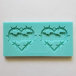 May include: A turquoise silicone mold with two heart-shaped cavities. Each heart has a barbed wire design around the edge and the word "Is this Love" written inside.