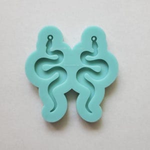 May include: A light blue silicone mould for making earrings. The mould has two snake-shaped cavities with holes for earring hooks.