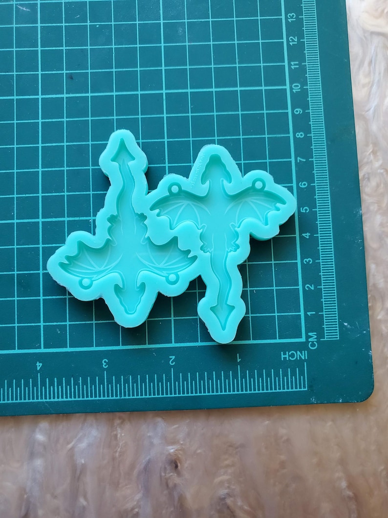 May include: A light blue silicone mold for making dragon-shaped resin ornaments. The mold has two dragon shapes, each with wings and a tail.