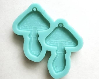 May include: A light blue silicone mold for making resin mushroom earrings. The mold has two cavities, each shaped like a mushroom with a stem and a cap.