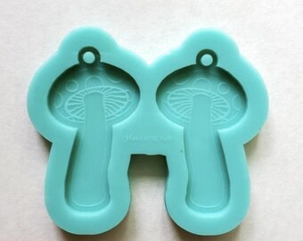 May include: A light blue silicone mold for making mushroom-shaped earrings. The mold has two cavities, each shaped like a mushroom with a stem and a cap with a detailed design.