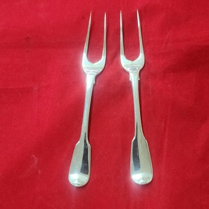 May include: Two silver forks with ornate handles on a red velvet background.