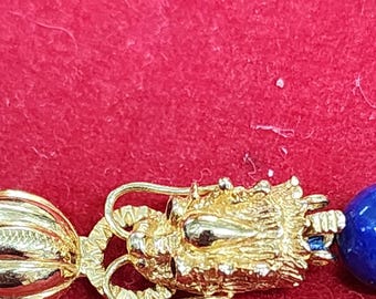 May include: A gold-toned necklace with a blue gemstone bead and a decorative gold clasp featuring a detailed design.